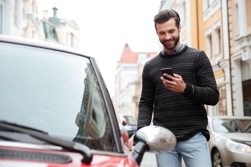 A man on his way to his car smiling at his smartphone.
