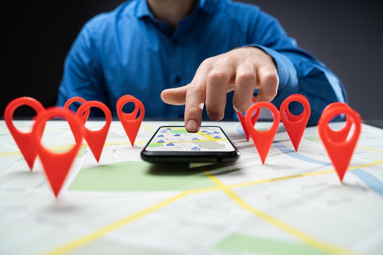 A man touching a navigation app on his phone that lies on a physical map with red pins highlighting important locations.