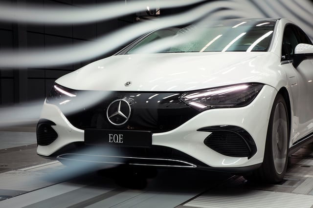 A closeup of a white Mercedes-Benz EQE with some white light beams which represent speed.