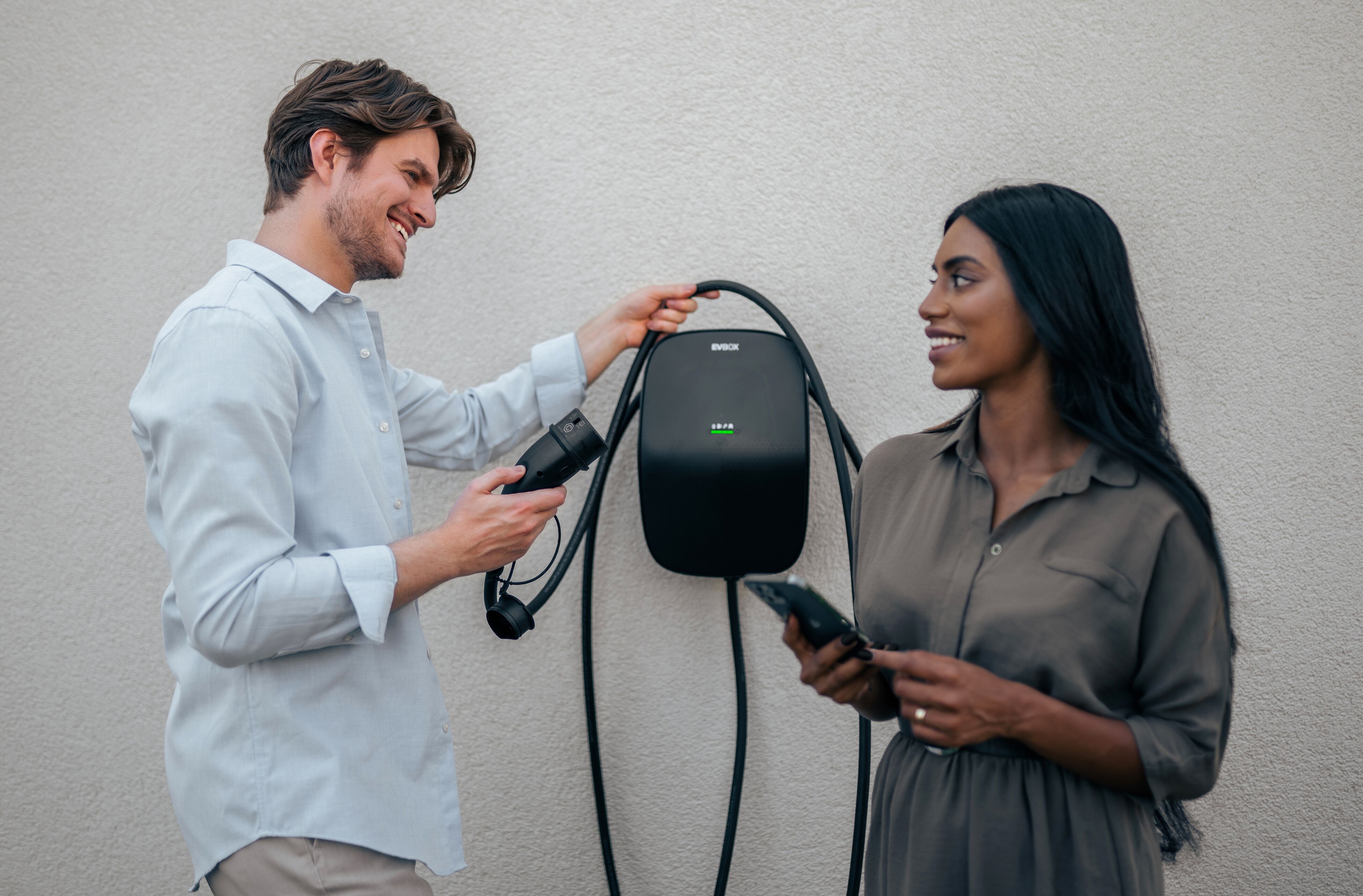 A couple standing in front of a mounted EVBox Livo AC home charging station.