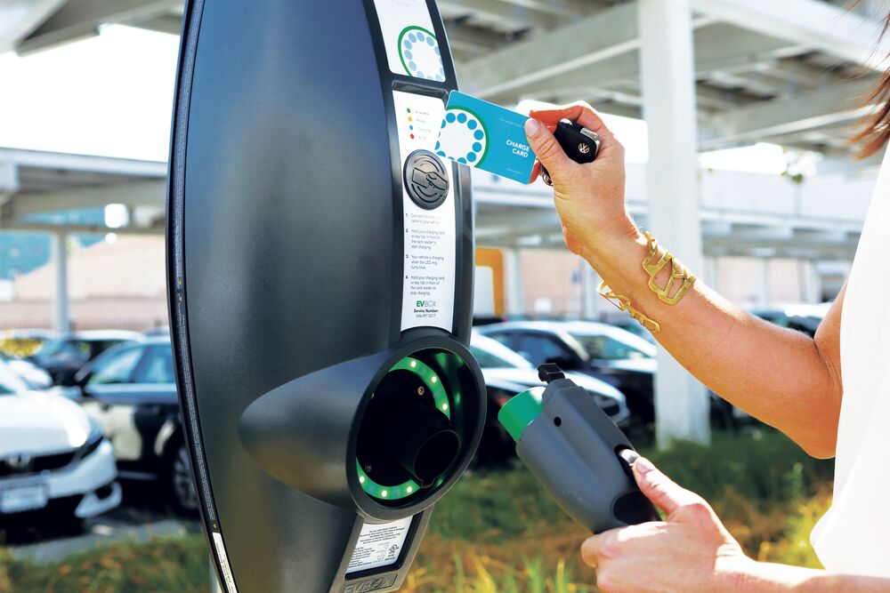 A woman going going to plug in her electric car cable into an EVBox BusinessLine, she also has an EVBox charge card in her right hand