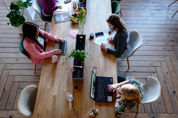 A birds eye view of a long wooden table in a communal working space, with several people working on their laptops