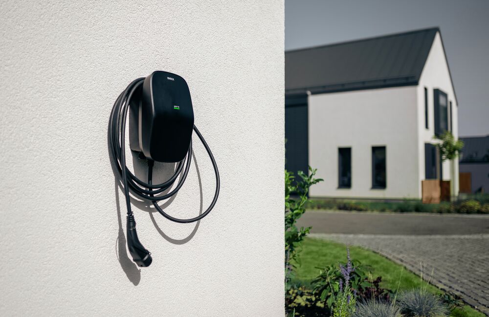 EVBox Livo socket on a wall. In the background, there is a residential house and plants.