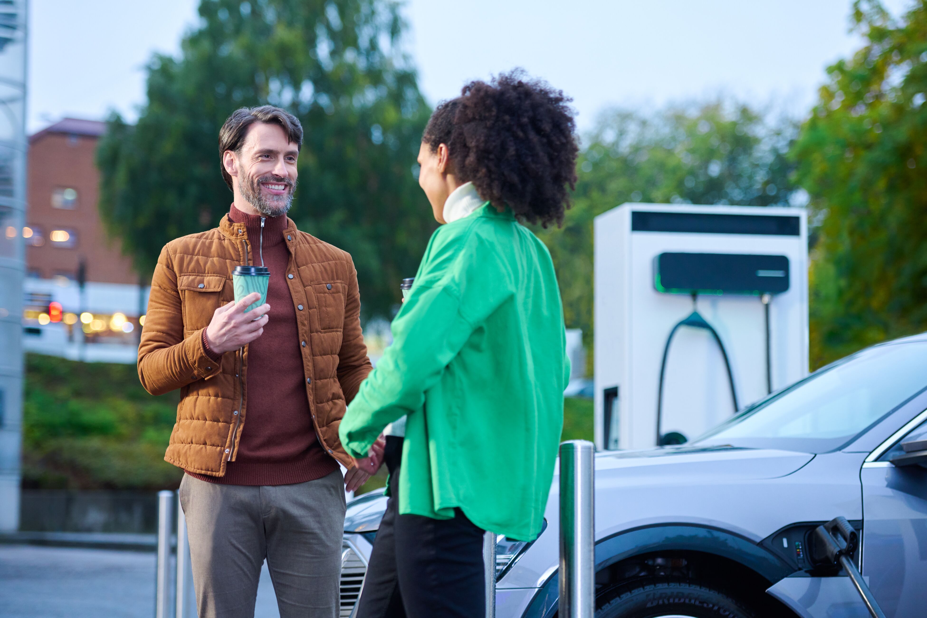 Un homme et une femme prennent un café pendant que leurs voitures sont rechargées par une station de recharge Dc modulaire EVBox Troniq.