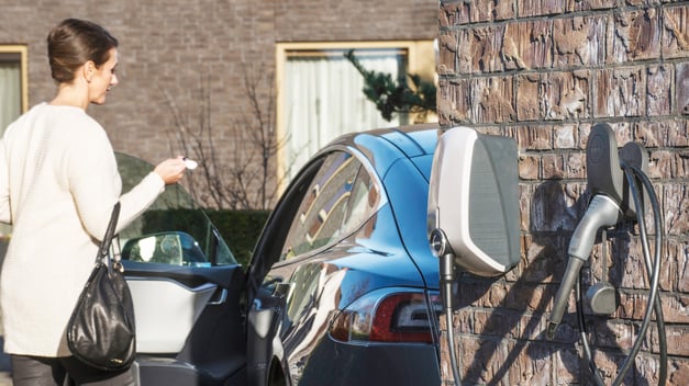 Een vrouw stapt in haar elektrische auto en heeft thuis een EVBox Elvi-laadpaal aan de buitenkant van haar huis.