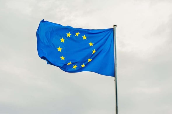 The European flag raised with a grey-sky backdrop.