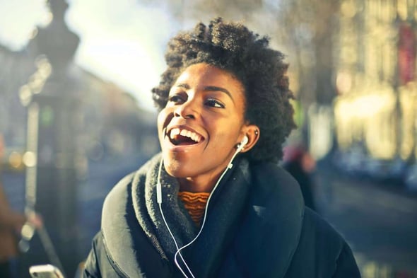 A young woman making her way through a city on foot, while listening to music on a sunny day during fall.