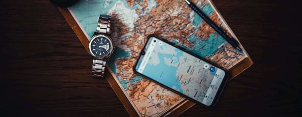 A watch and smarthphone showing a detailed map on top of an physical map of Europe representing the old and new in one image. 