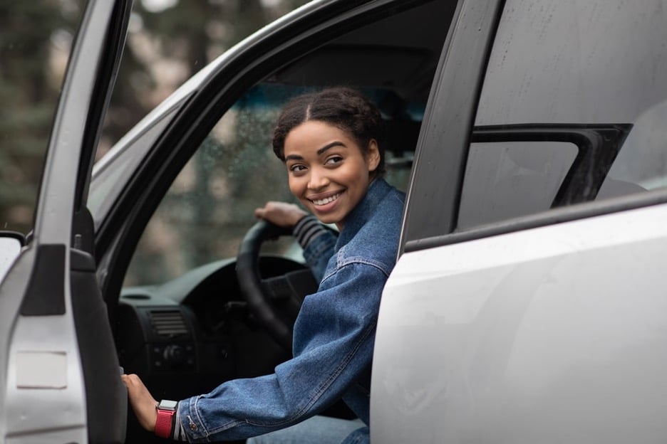 Vrouw achter het stuur houdt lachend autodeur open 
