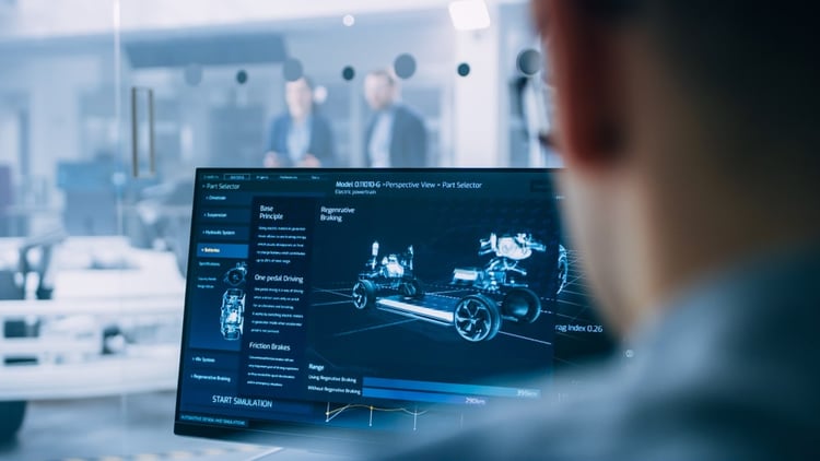 Looking over the shoulder of an engineer in a lab who's staring at his desktop screen showing a blueprint of an electric car.