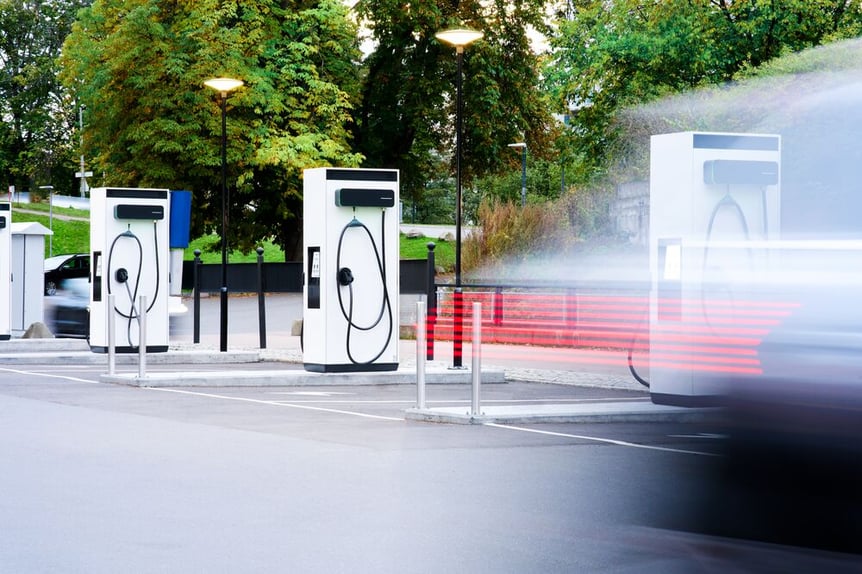 A parking lot with three EVBox Troniq Modular fast-charging stations and the movement of a car passing by captured with a slow shutterspeed.