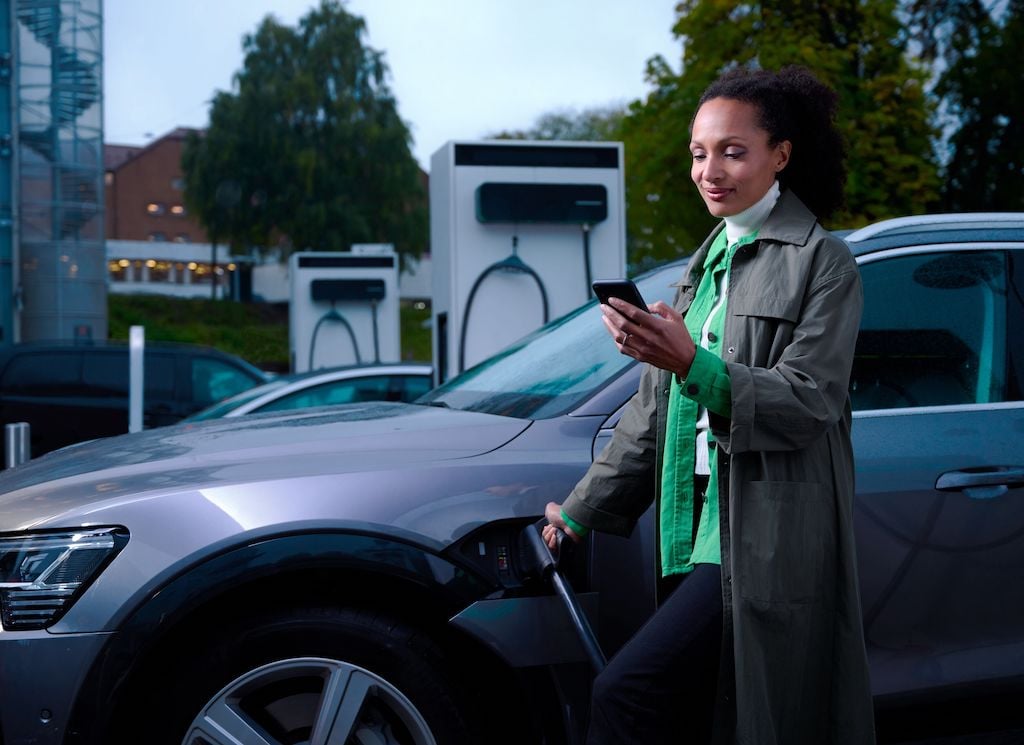 A lady charging her car at an EVBox Troniq Modular fast charging station while checking her smartphone.