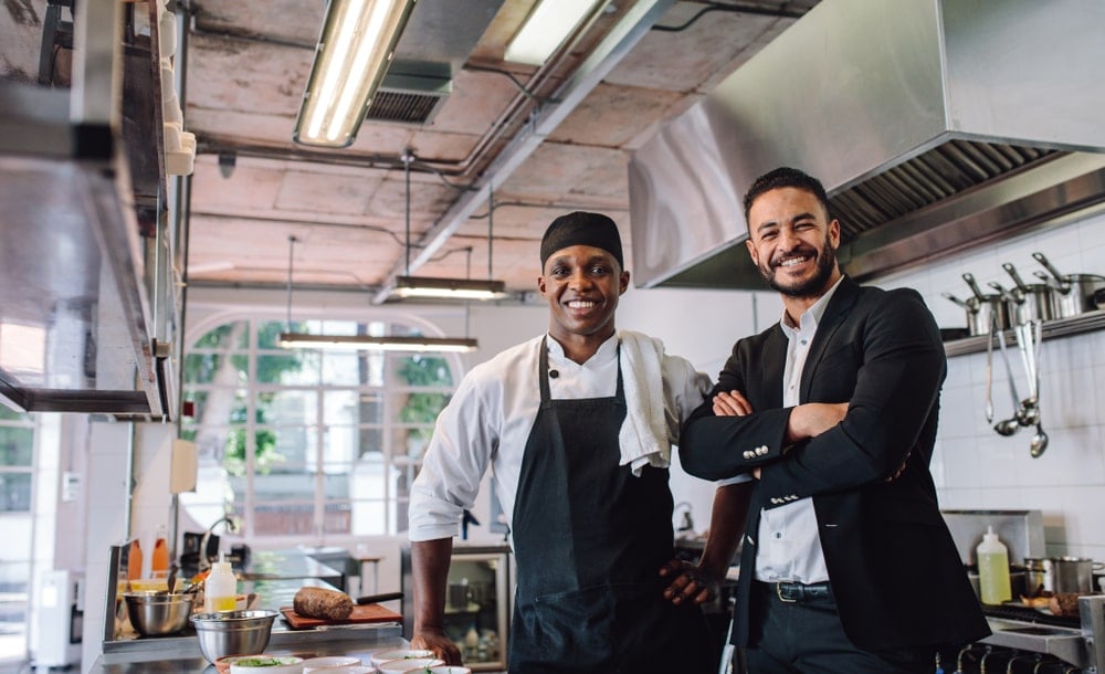 A chef and a business man standing in a kitchen.