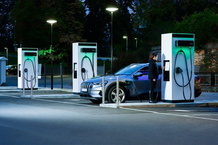 A lady charging her car at an EVBox Troniq Modular fast charging station at night.