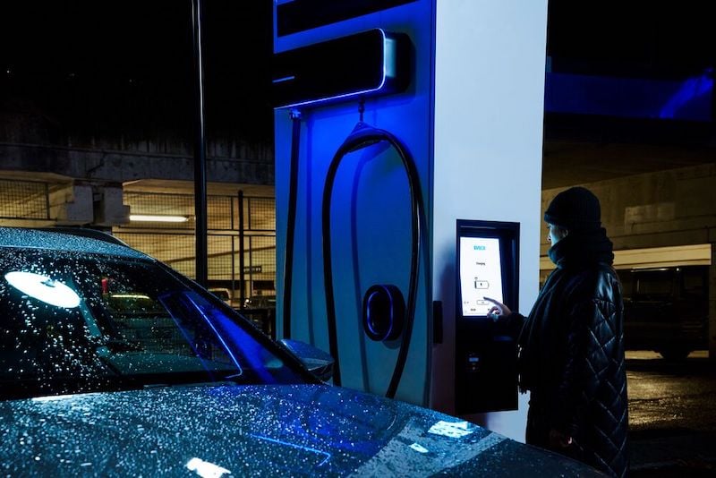 A woman is charging her EV using a led-lit-up EVBox Troniq Modular in a rainy night.