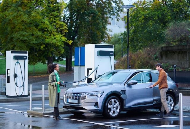 A couple are charging their electric car while talking to each other.