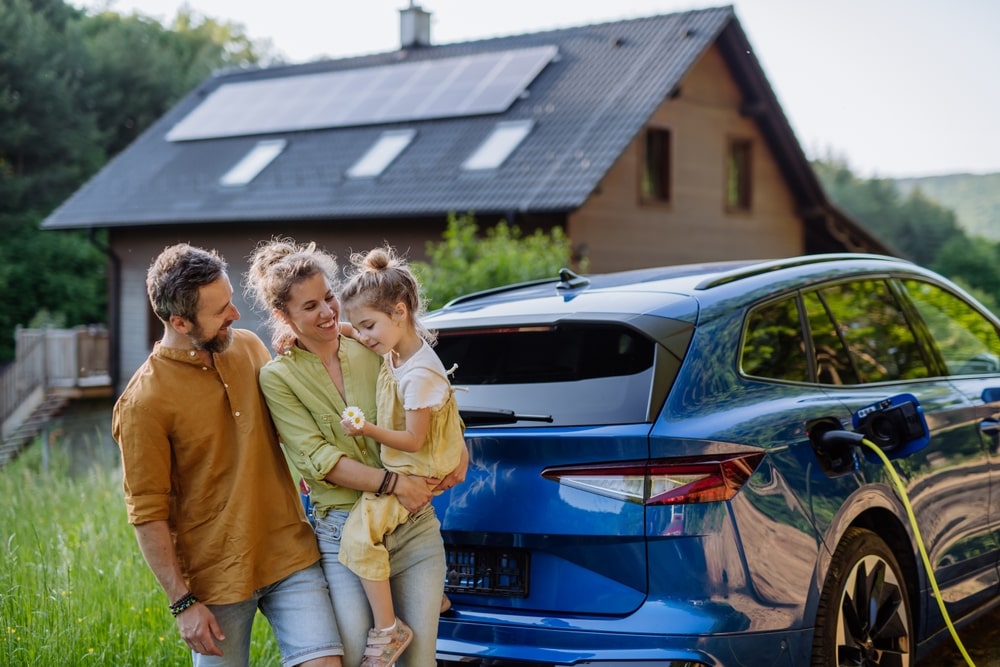 A family standing next to their electric car charging on solar power at home.