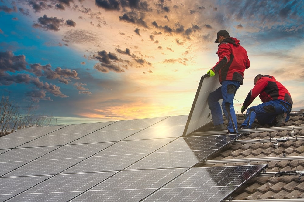 Professionals installing solar panels on a rooftop at sunset.