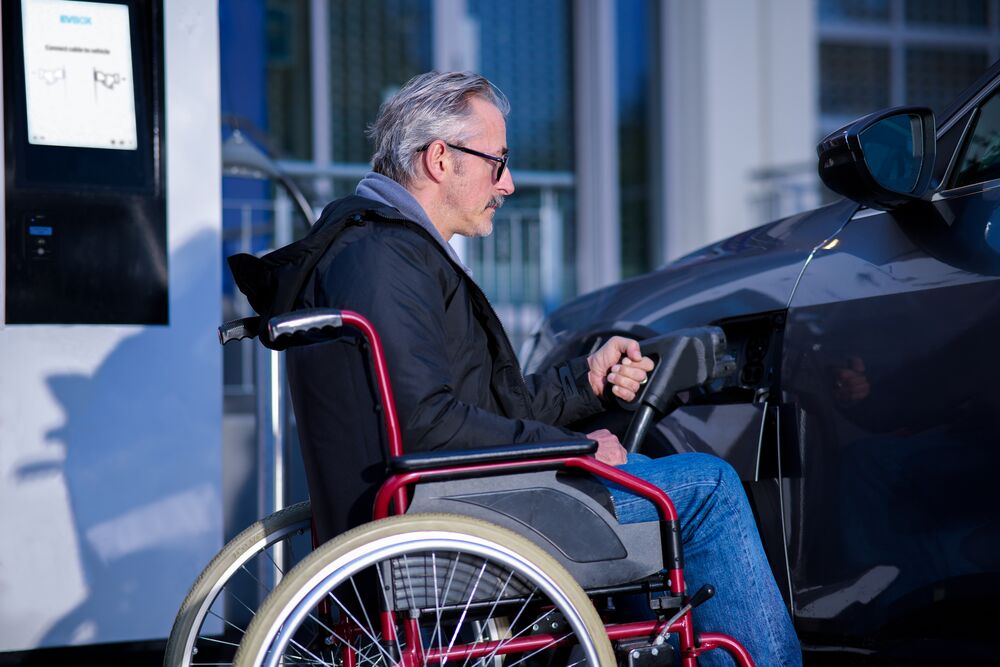 A man sitting on a wheelchair is charging his EV using EVBox Troniq Modular charging station..