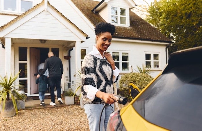 A woman is charging her EV while her husband and kid are walking to their home.