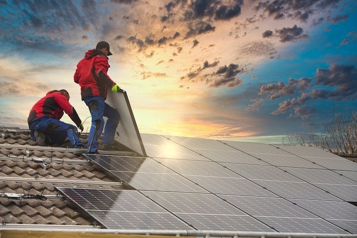 Two technical specialists are installing solar panels on the roof.