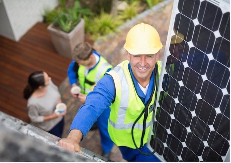 Two technicians are helping a woman install solar panels at her house
