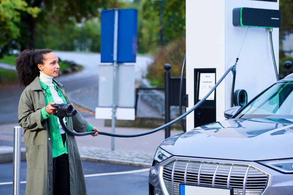 A woman pulls the cable of an EVBox Troniq Modular fast-charging station in front of her EV.
