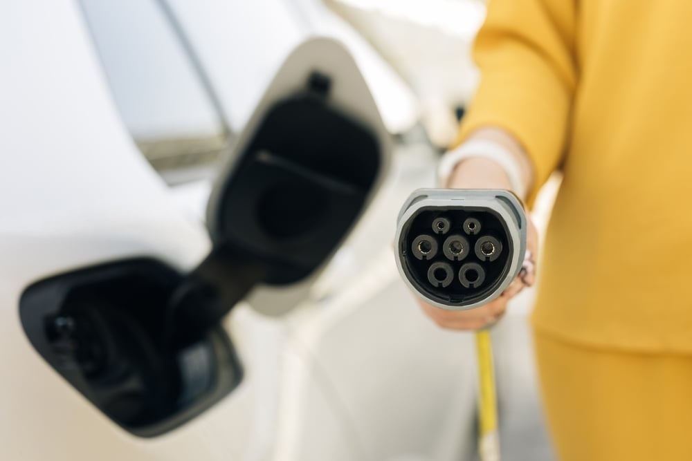 A woman holds an EV charging cable and plug next to the open charging port of an EV.