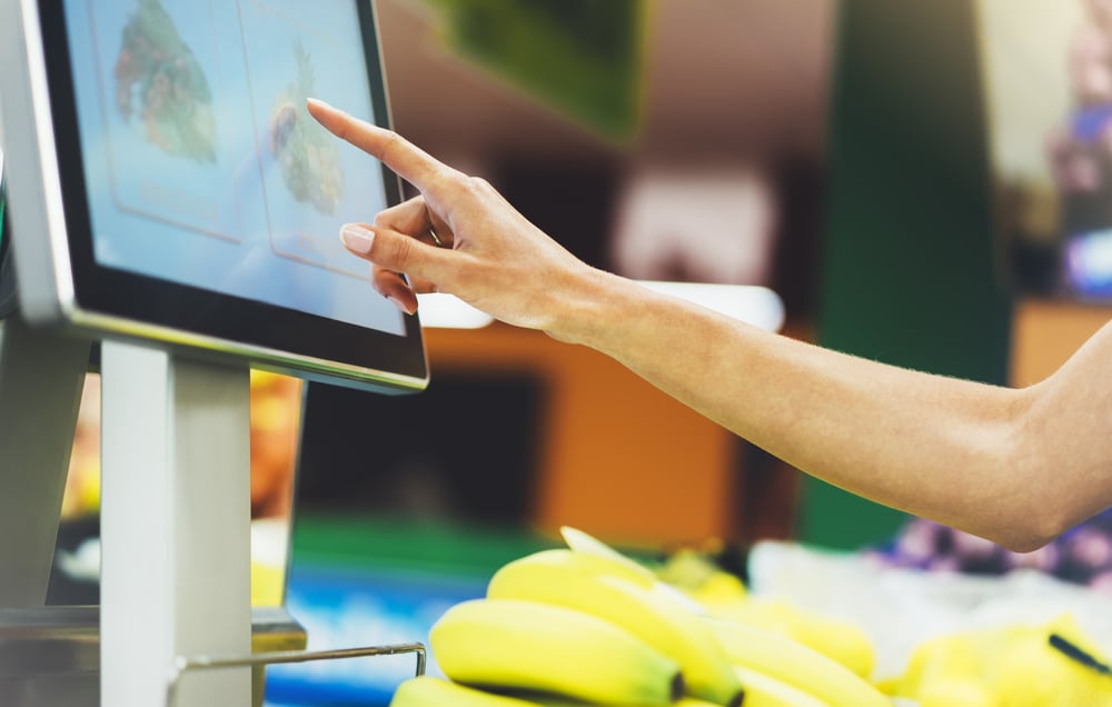 A woman selects the fruit icon on the screen of the fruit and vegetable scale at the grocery store as she weighs bananas.
