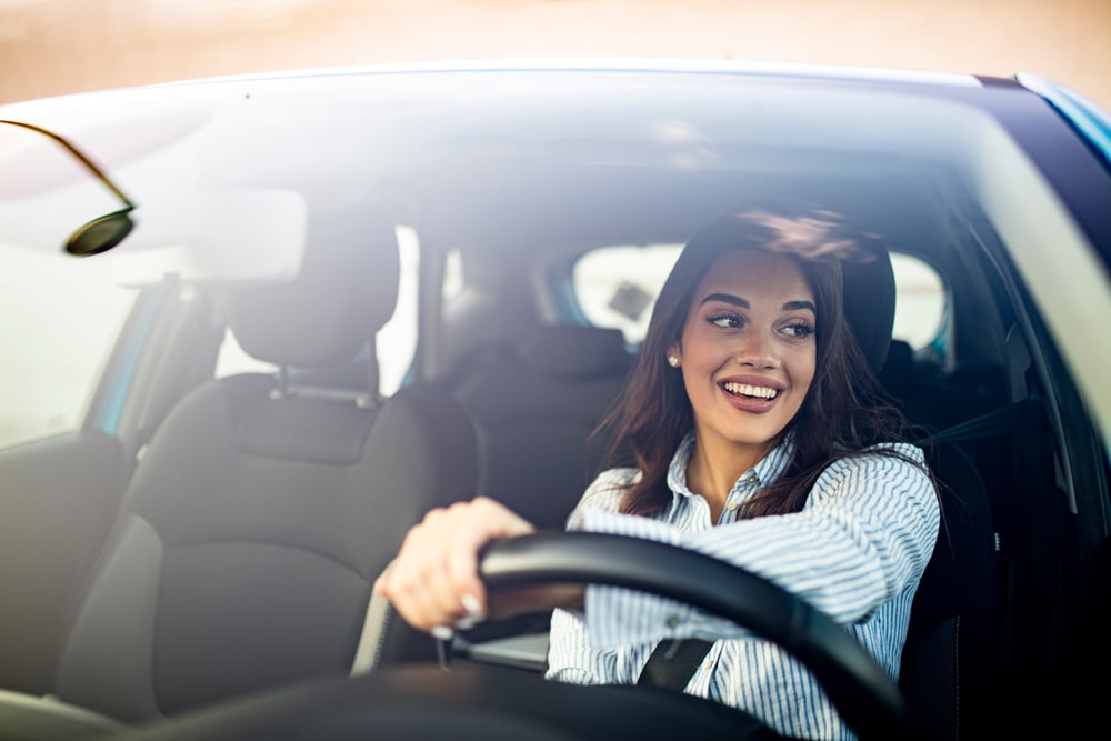 A smiling woman drives her car.