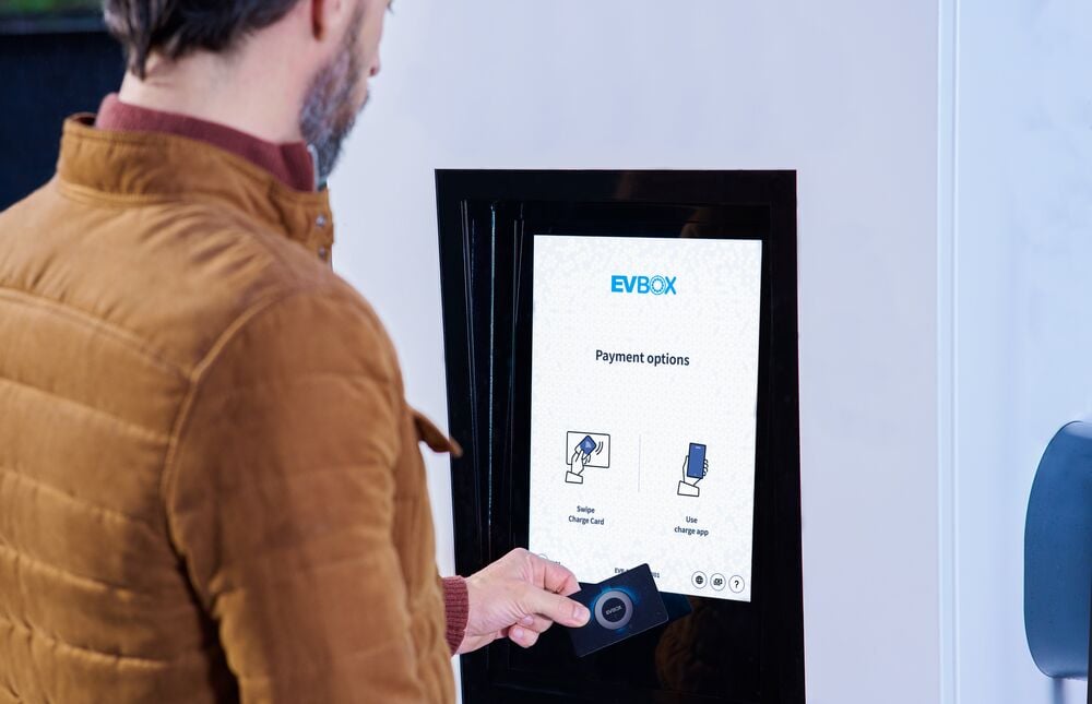 A man taps his RFID card on the screen of the EVBox Troniq Modular charging station to pay for his fast-charging session.