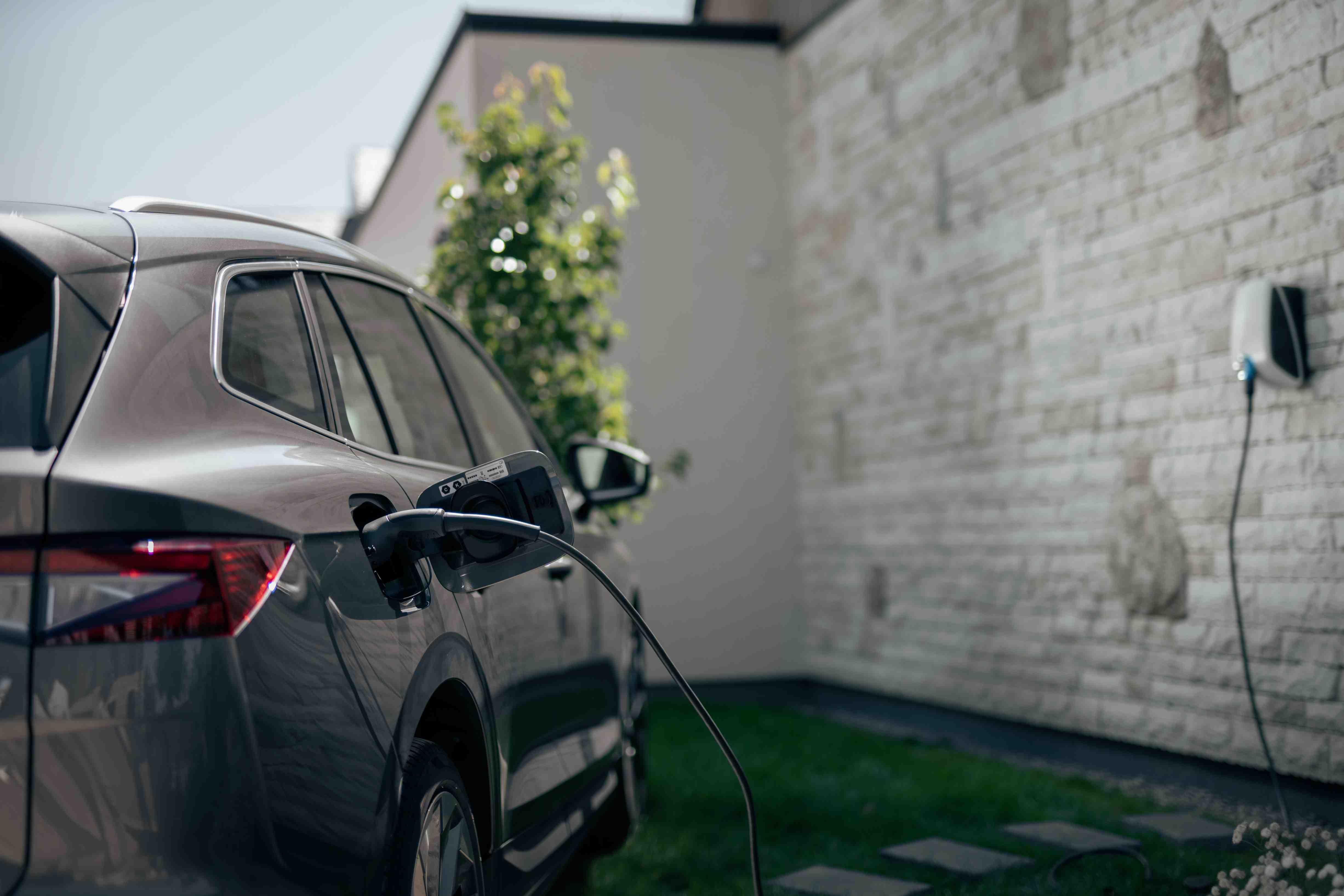An electric SUV parked in the driveway and is connected to the Elvi home charging station mounted on the brick wall.
