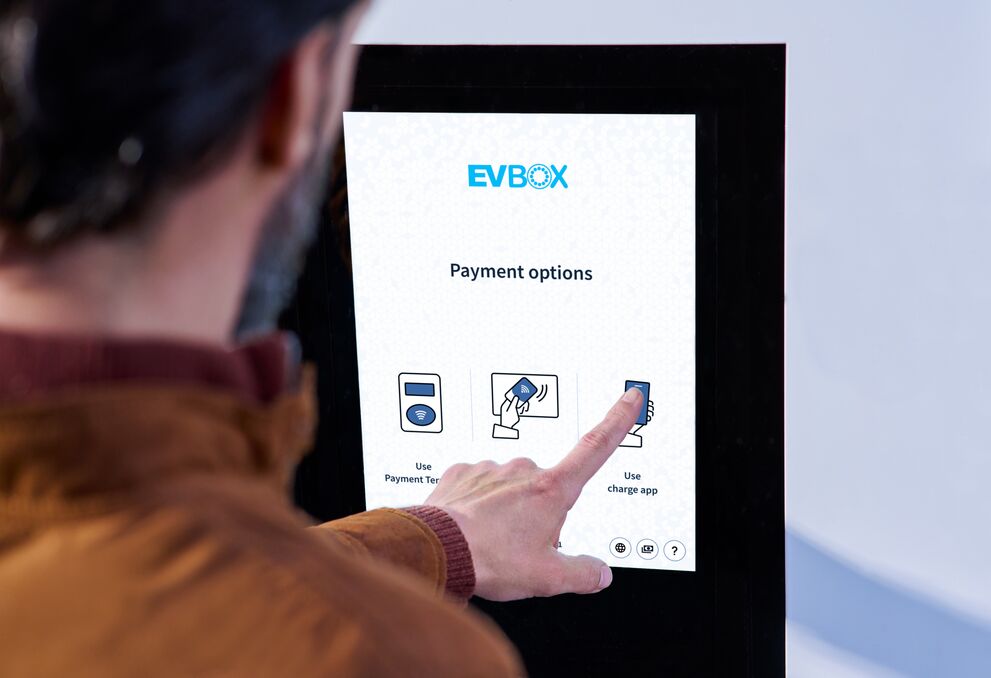 A man interacts with the screen of an EVBox Troniq High Power charging station. 