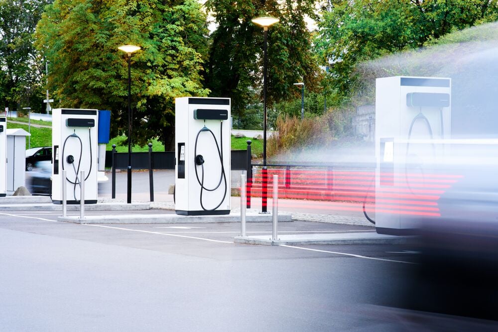 A car driving away quickly in a blurred motion in front of a parking area filled with EVBox Troniq Modular DC fast chargers.