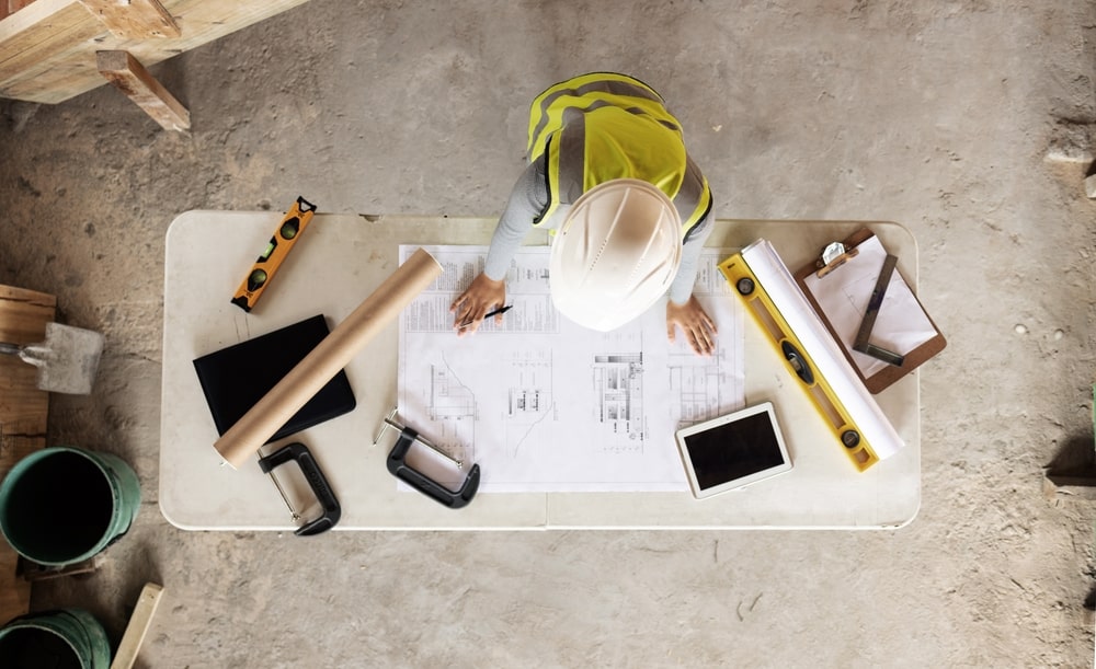 A Bird's-eye view of a man with a hard hat looking at a blueprint on a table.