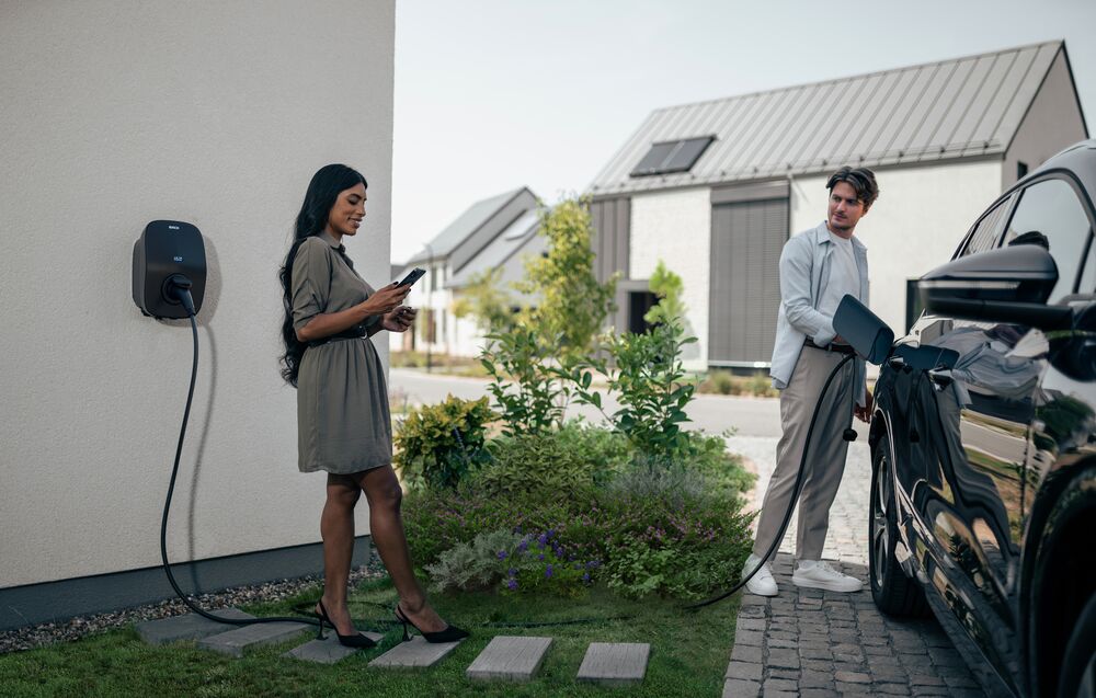 EVBox Livo charging station being used by a man while a woman looks at her phone at their house.