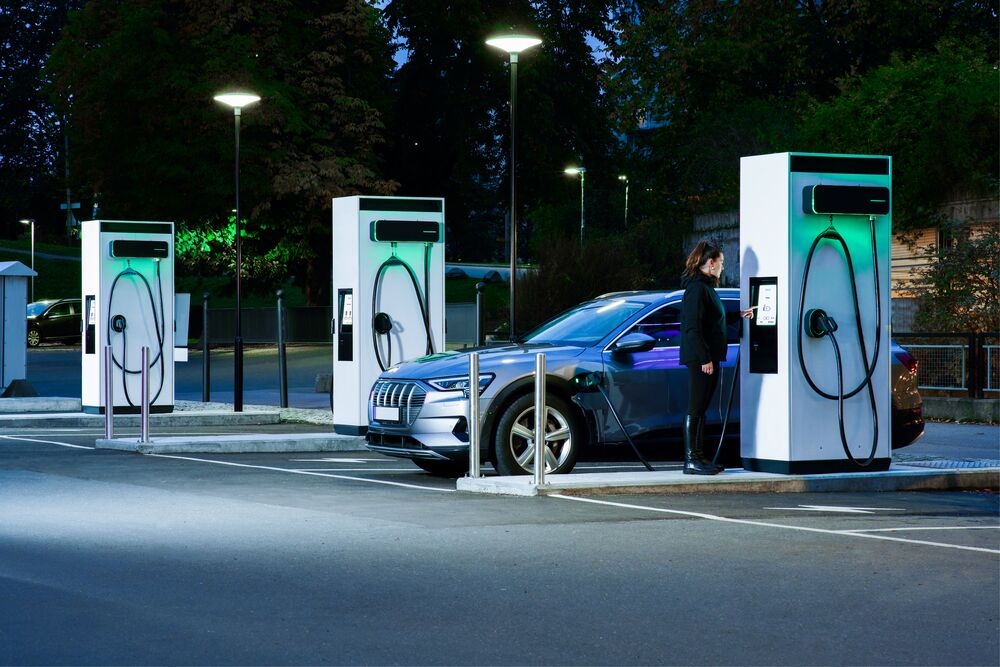 Three EVBox Troniq Modulars. A woman is using one of the charging stations to charge her electric car.