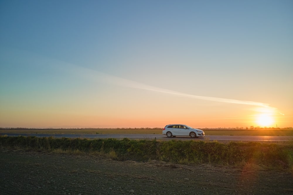 A white car driving in an empty road with a sunset in the background.
