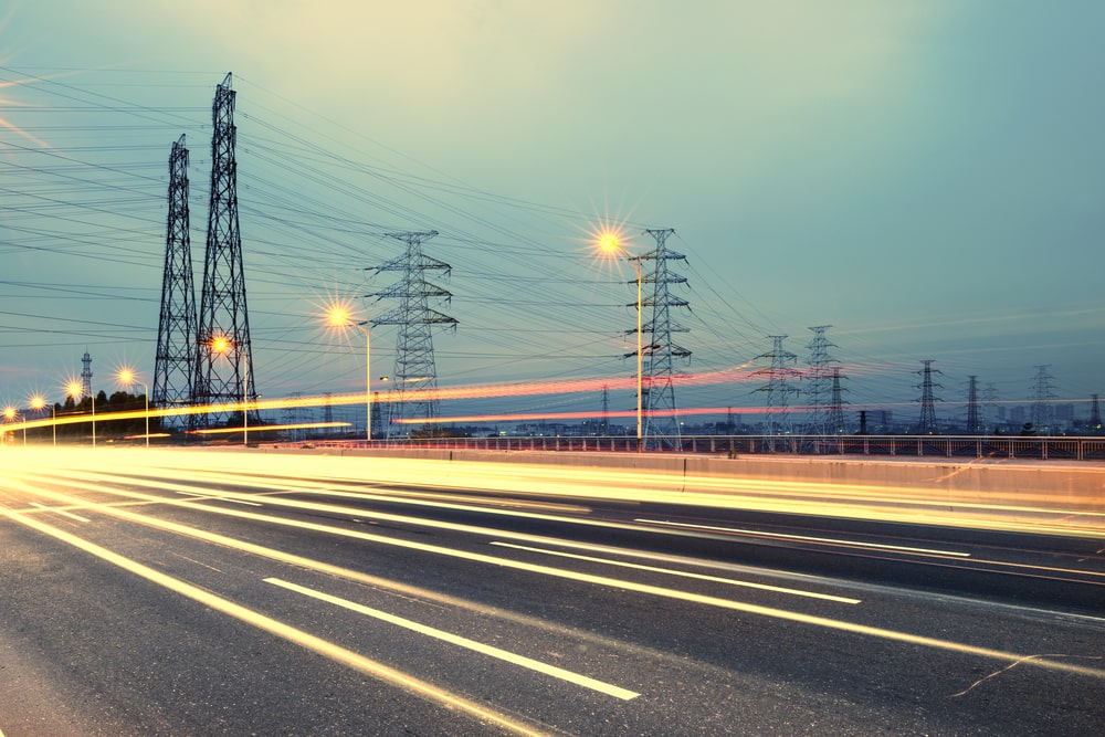 Cars passing by on highway, with high-voltage towers in the background.