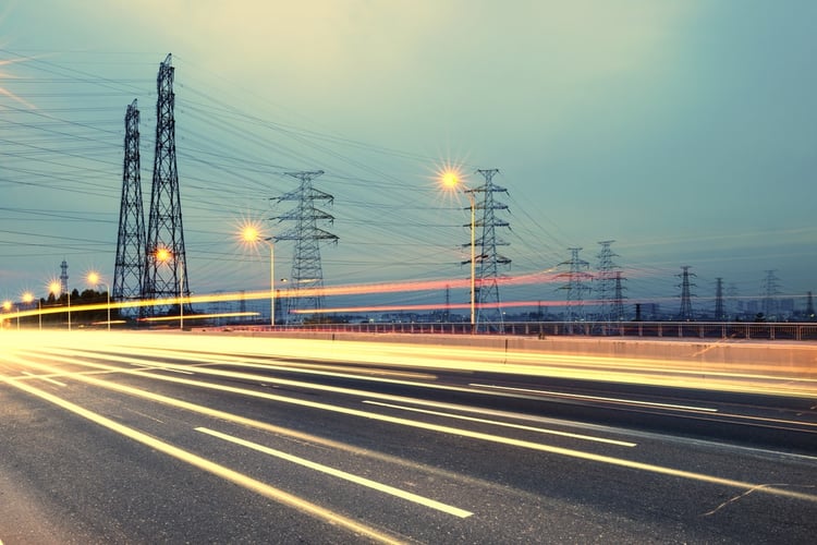 Cars driving by high-voltage towers.