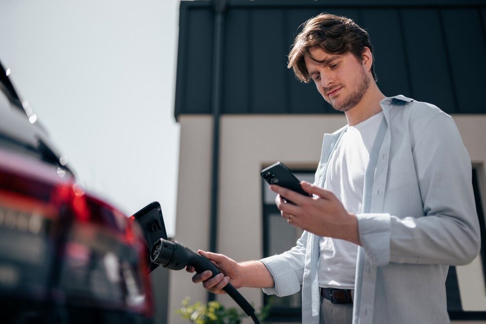 Man charging his car at home with EVBox Livo and using his EVBox Everon app to set his solar smart charging settings.