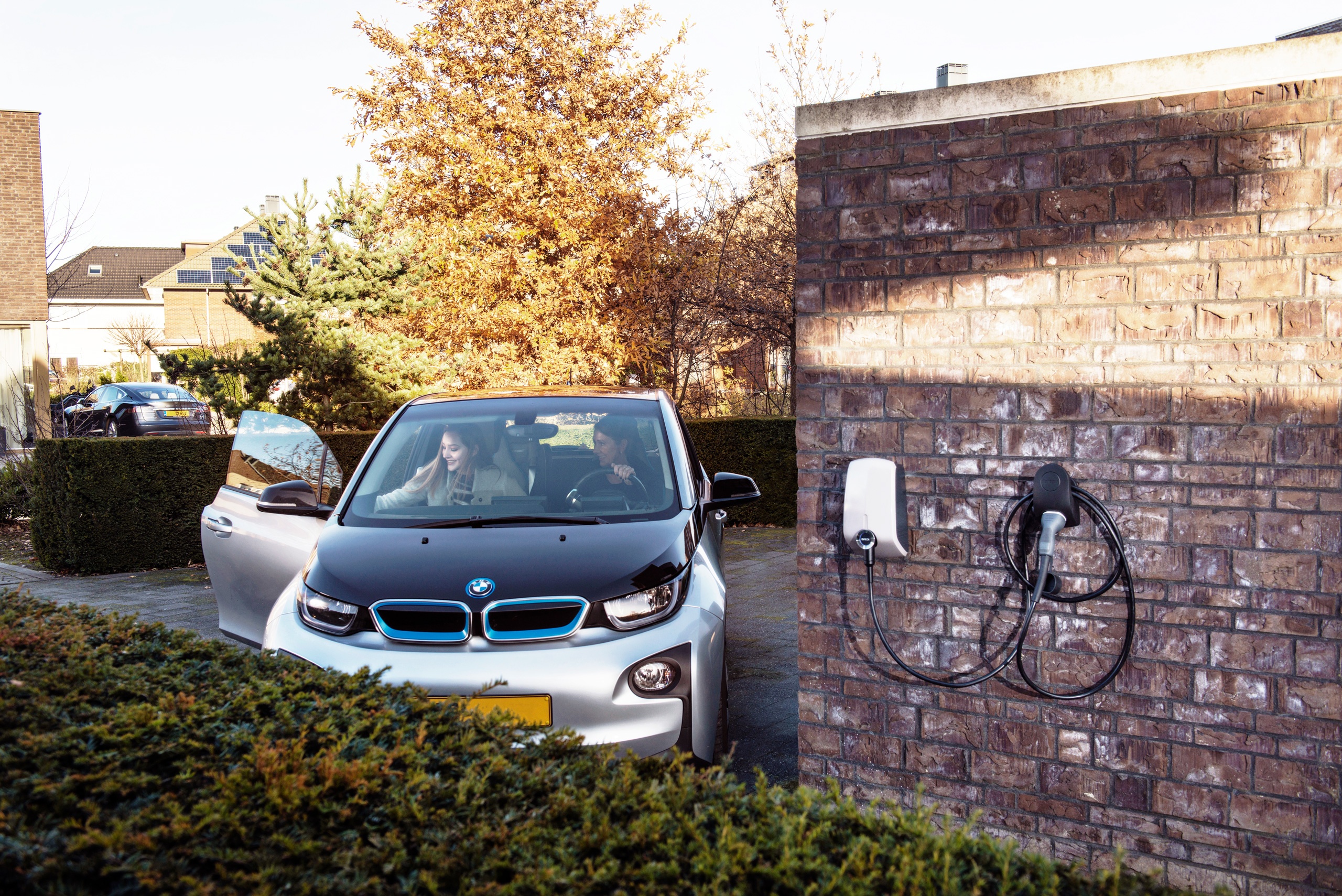 An electric BMW parking at a residential dwelling in the leafy suburbs next to a professionally installed EV charging station.