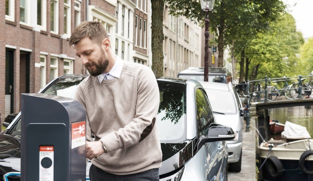 Ein halbwegs lässiger Mann lädt sein Elektroauto an einer öffentlichen Ladestation in Amsterdam auf.