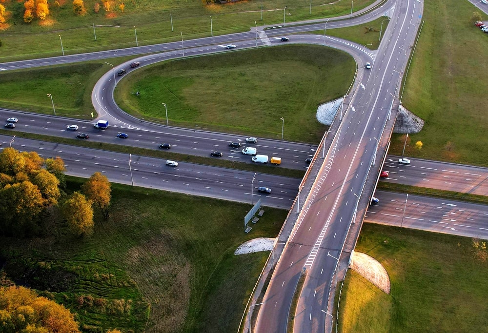 Highway along a green field with a road bridge and traffic interchange, view from the air.