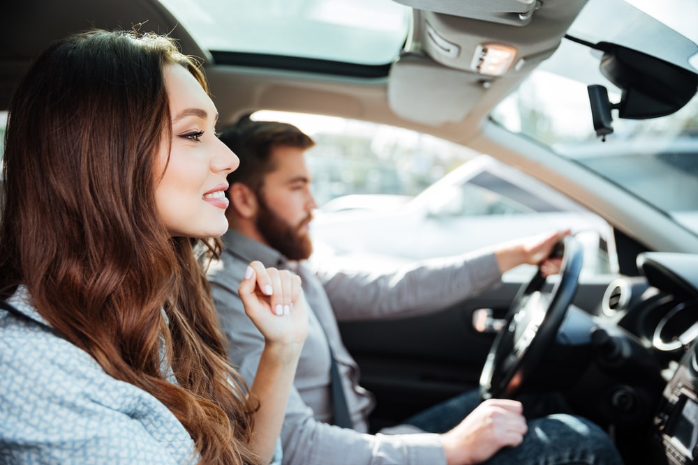 A man drives an EV while a woman sits in the passenger seat.