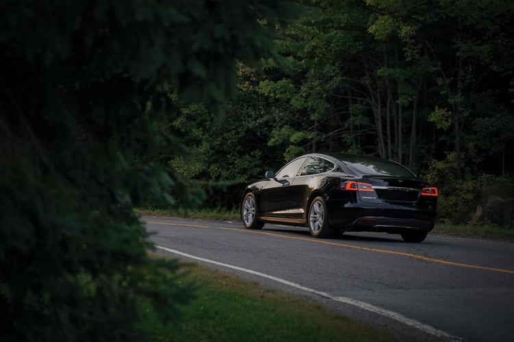 Voiture noire roulant sur une route entourée d'arbres.