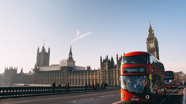 Two double-decker buses driving through London across a bridge
