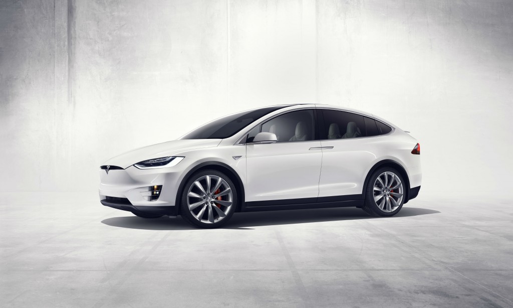 A Tesla model X sitting against a concrete backdrop.