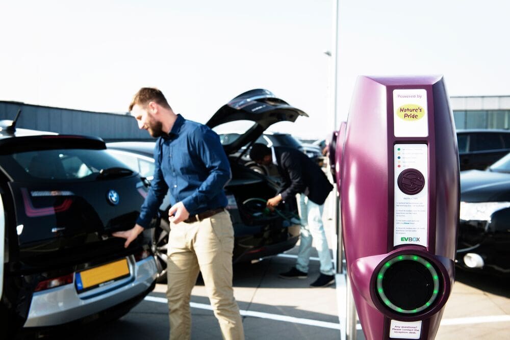 EVBox BusinessLine Ladestation, personalisiert mit einem Firmenbranding. Im Hintergrund ist ein Geschäftsmann zu sehen, der den Kofferraum seines Autos öffnet.