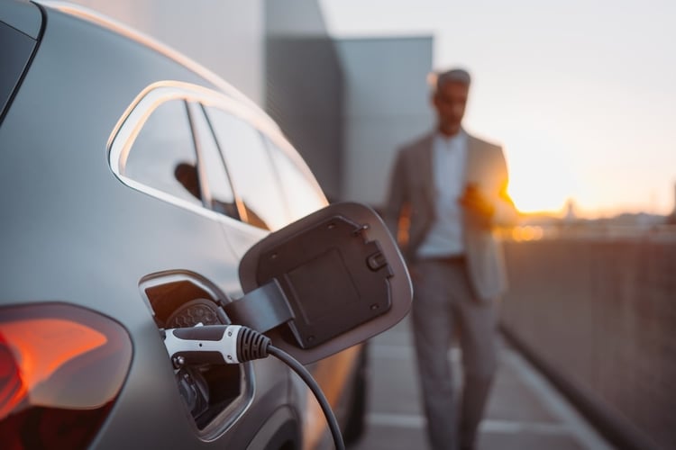 Une voiture électrique en charge. Il y a un homme d'affaires qui marche vers la voiture en arrière-plan.